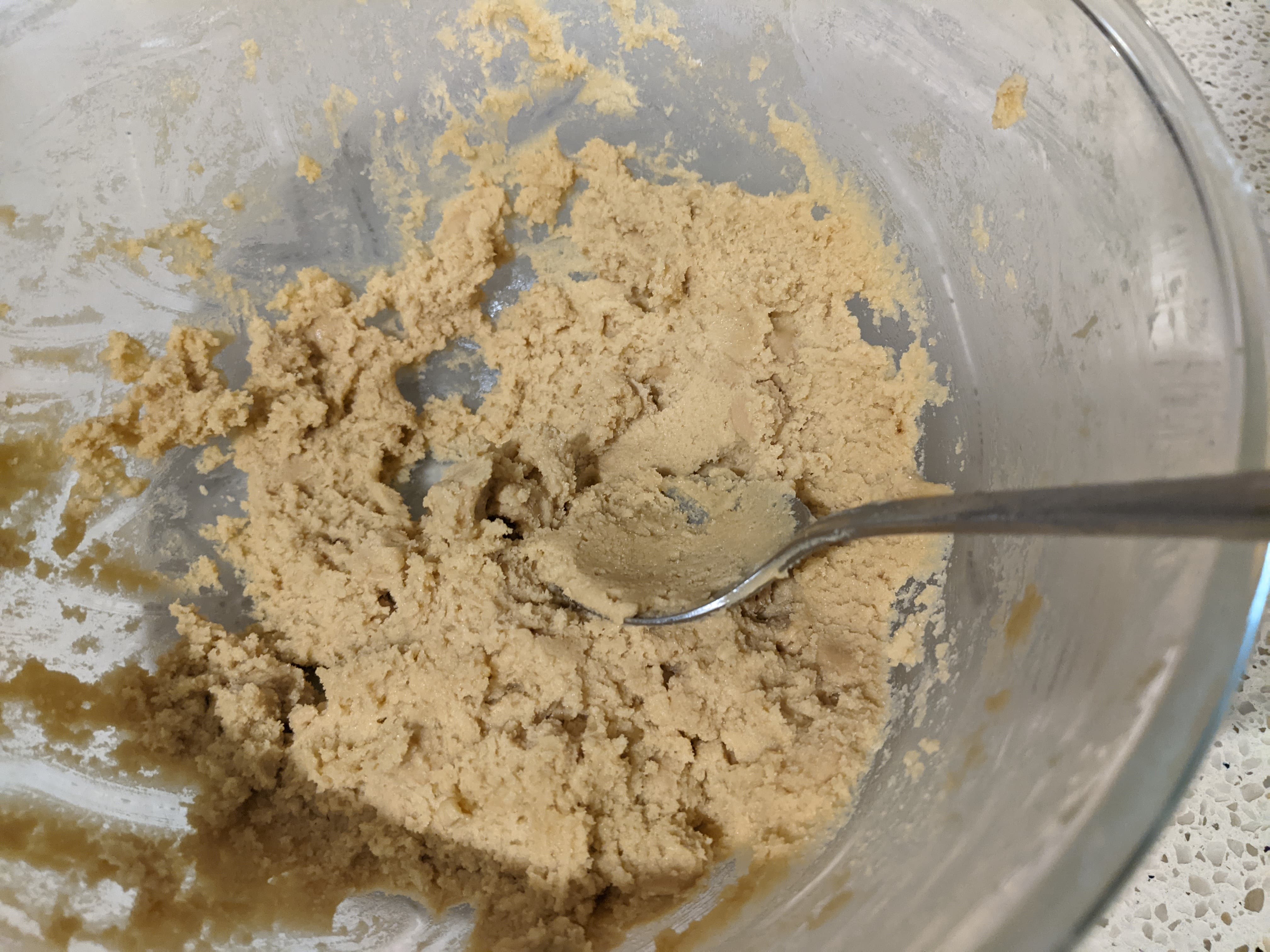 A glass bowl with some cookie dough and a spoon