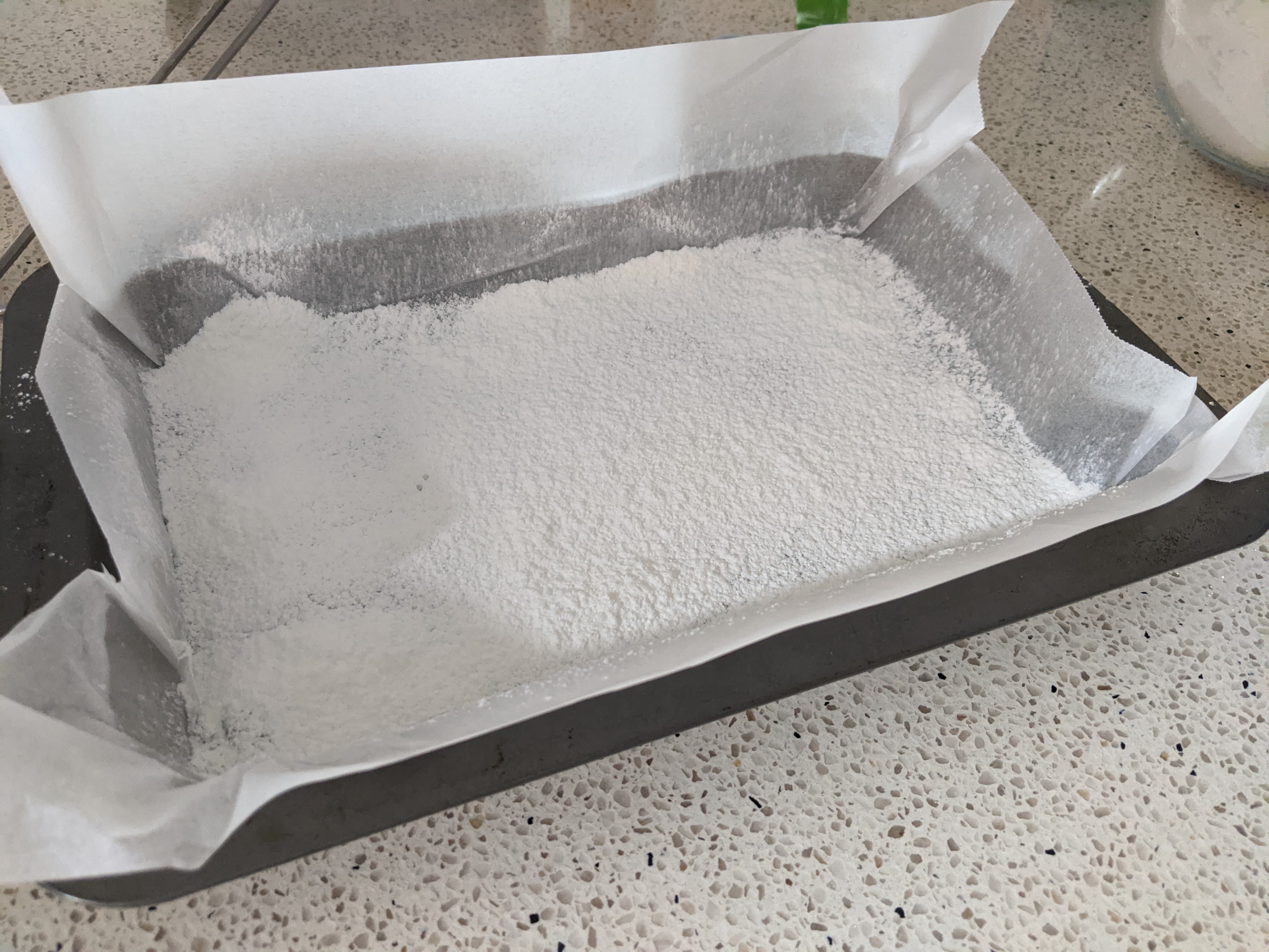A rectangular baking pan lined with baking paper and dusted