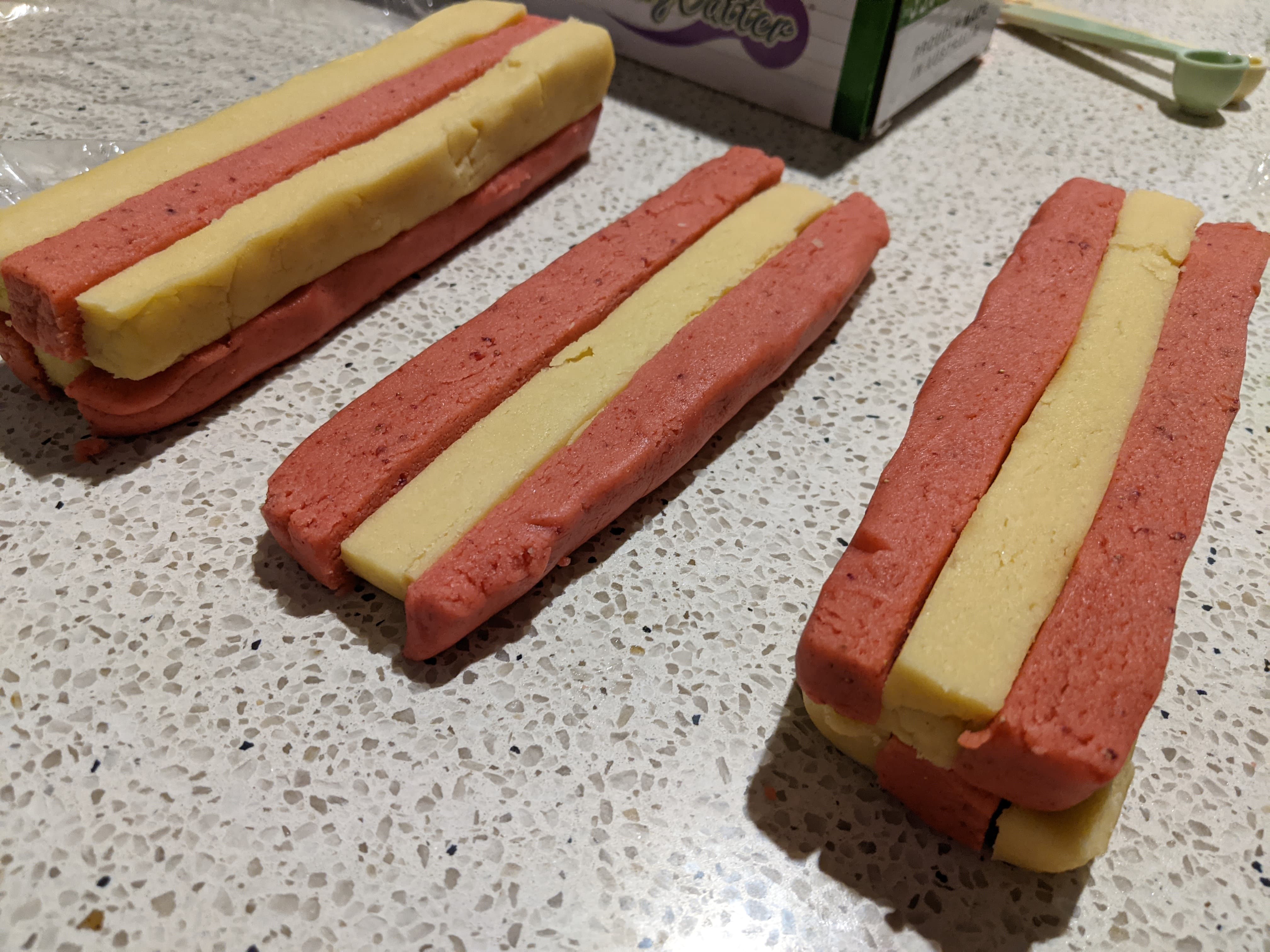 Red and white logs of cookie dough in the process of being spliced together so the colours alternate
