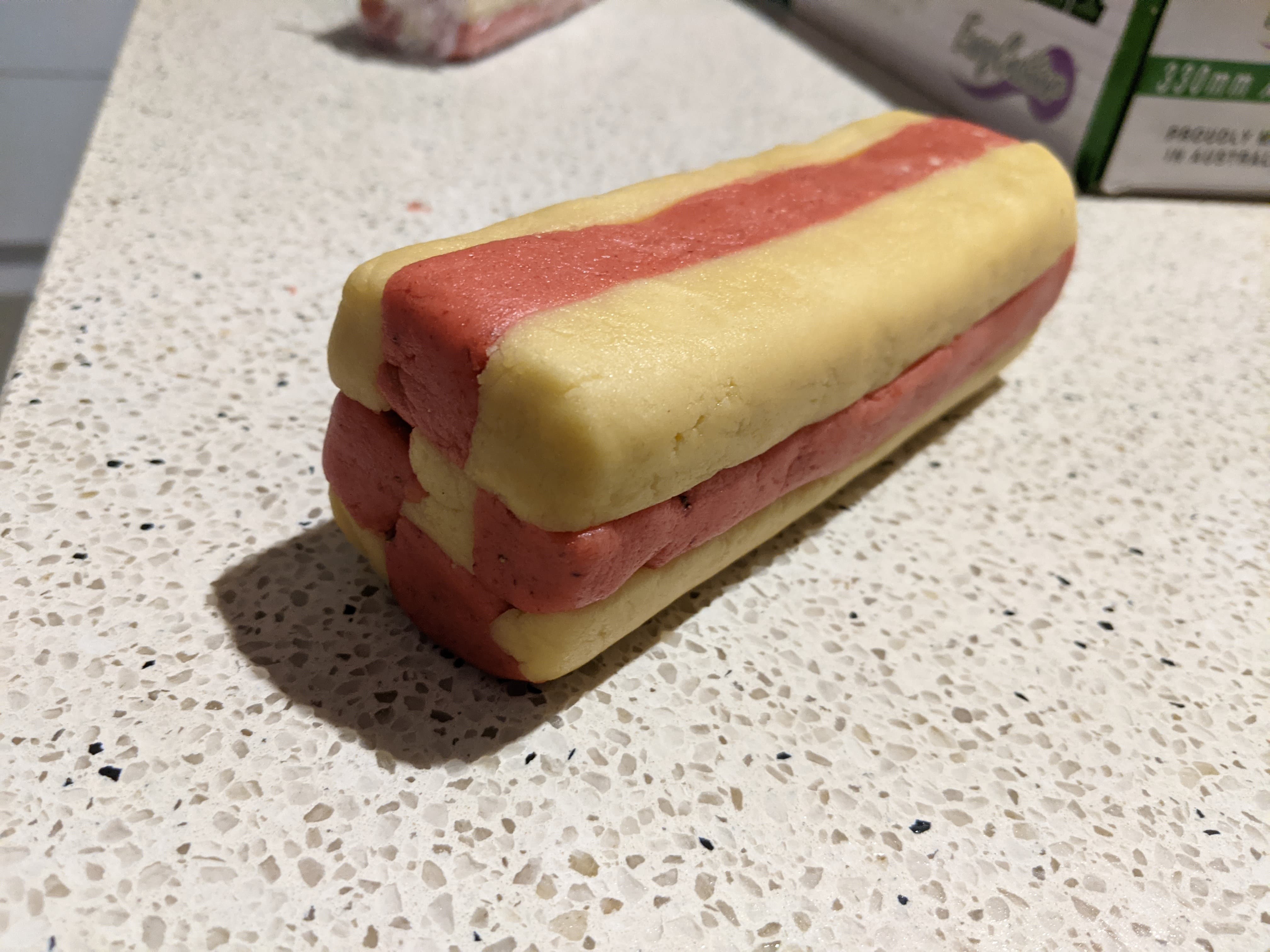 A log of cookie dough that has been spliced from two different colours into a checkerboard pattern