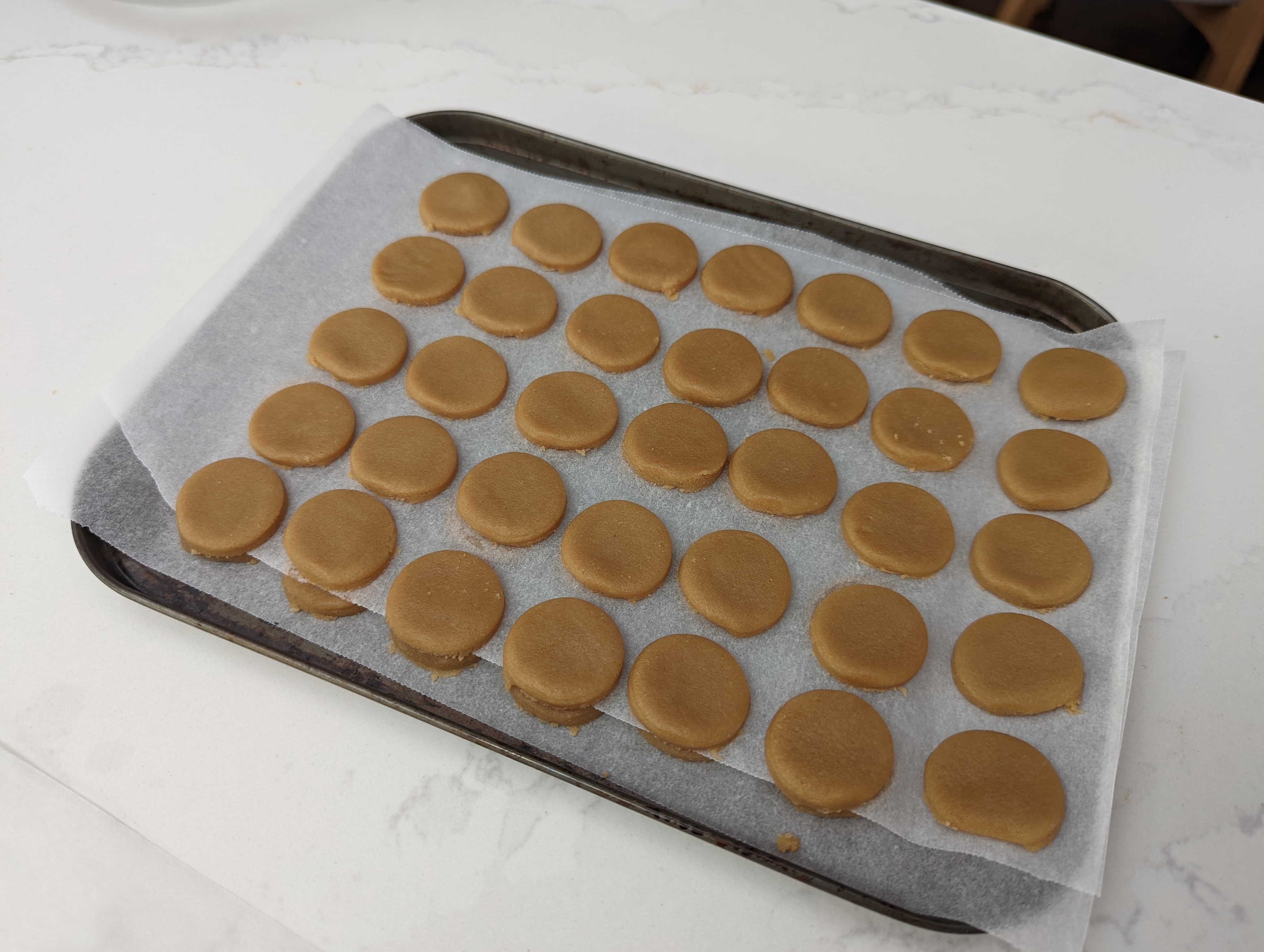 A baking tray with 2 layers of baking paper, each filled with rounds of dark brown craquelin dough