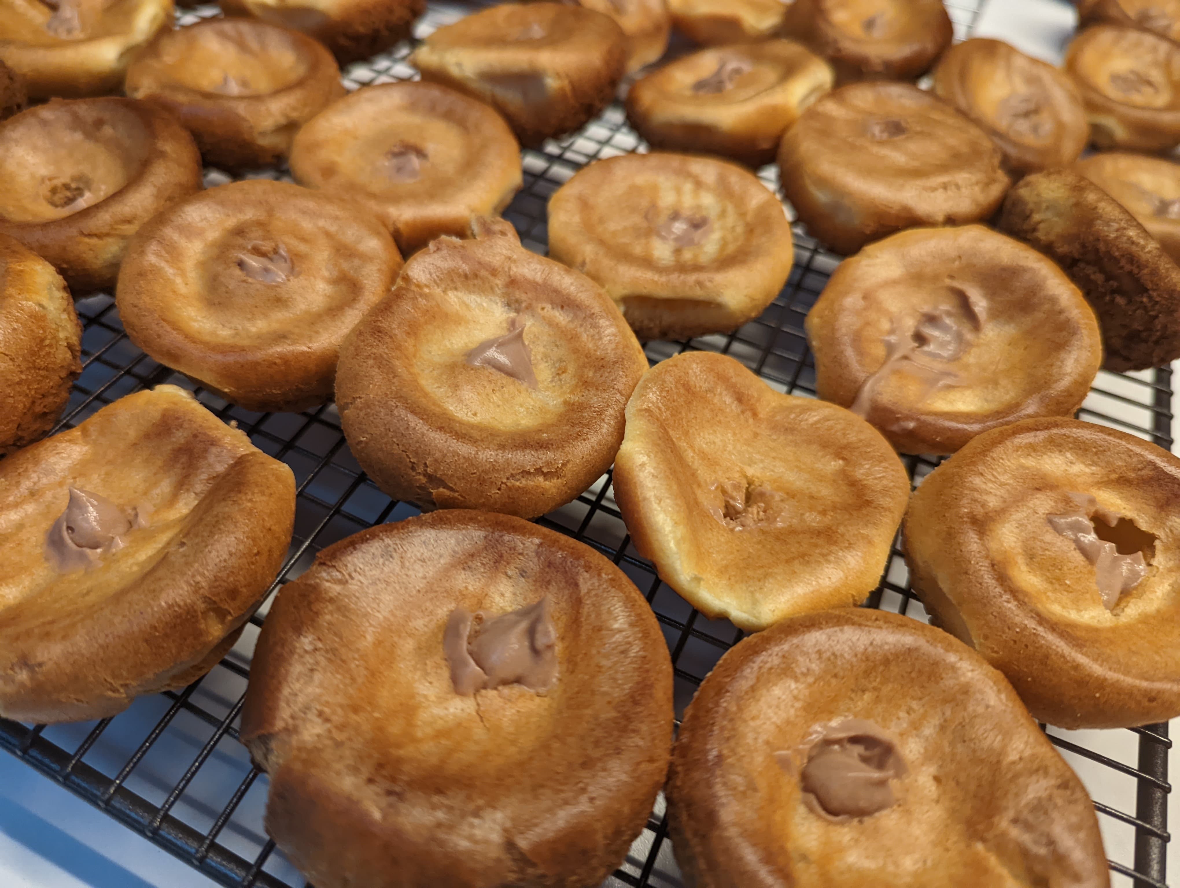 Several upturned choux pastries on a wire rack, with chocolate cream in each